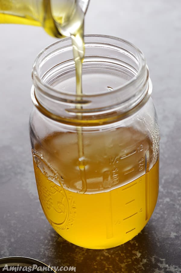 Pouring ghee into a mason jar with the lid on the side.