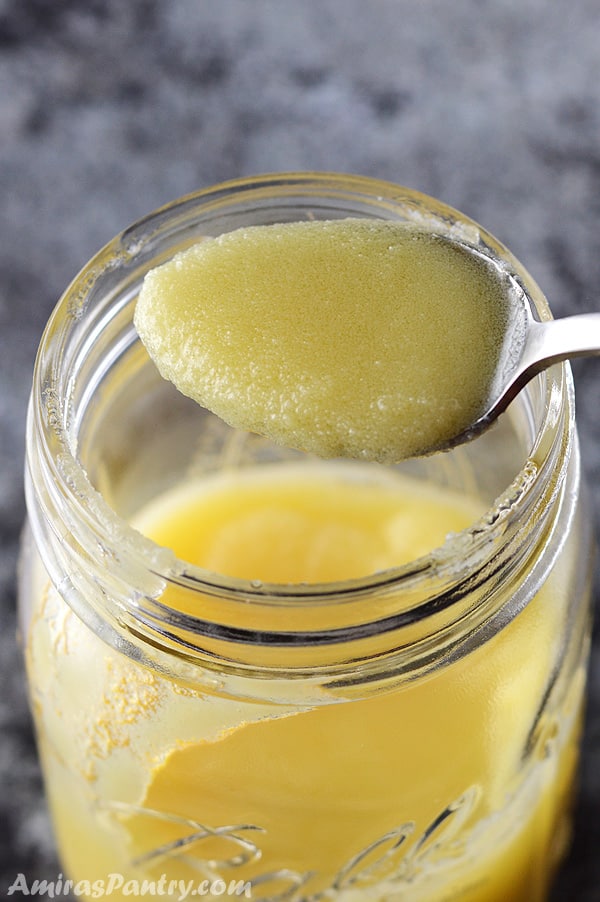 A spoon scooping some solidified ghee from the jar.