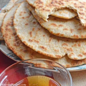 A stack of flatbread on a blue plate with a small bowl of honey.