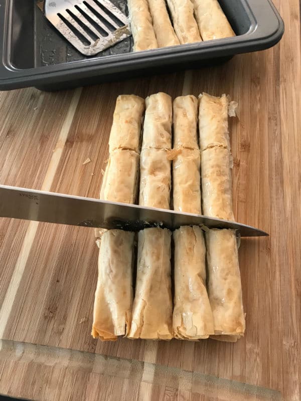 A wooden cutting board, with Baklava cut with knife