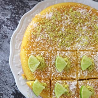 Revani cake placed on a white platter and decorated with lemon pieces, coconut and crushed pistachios