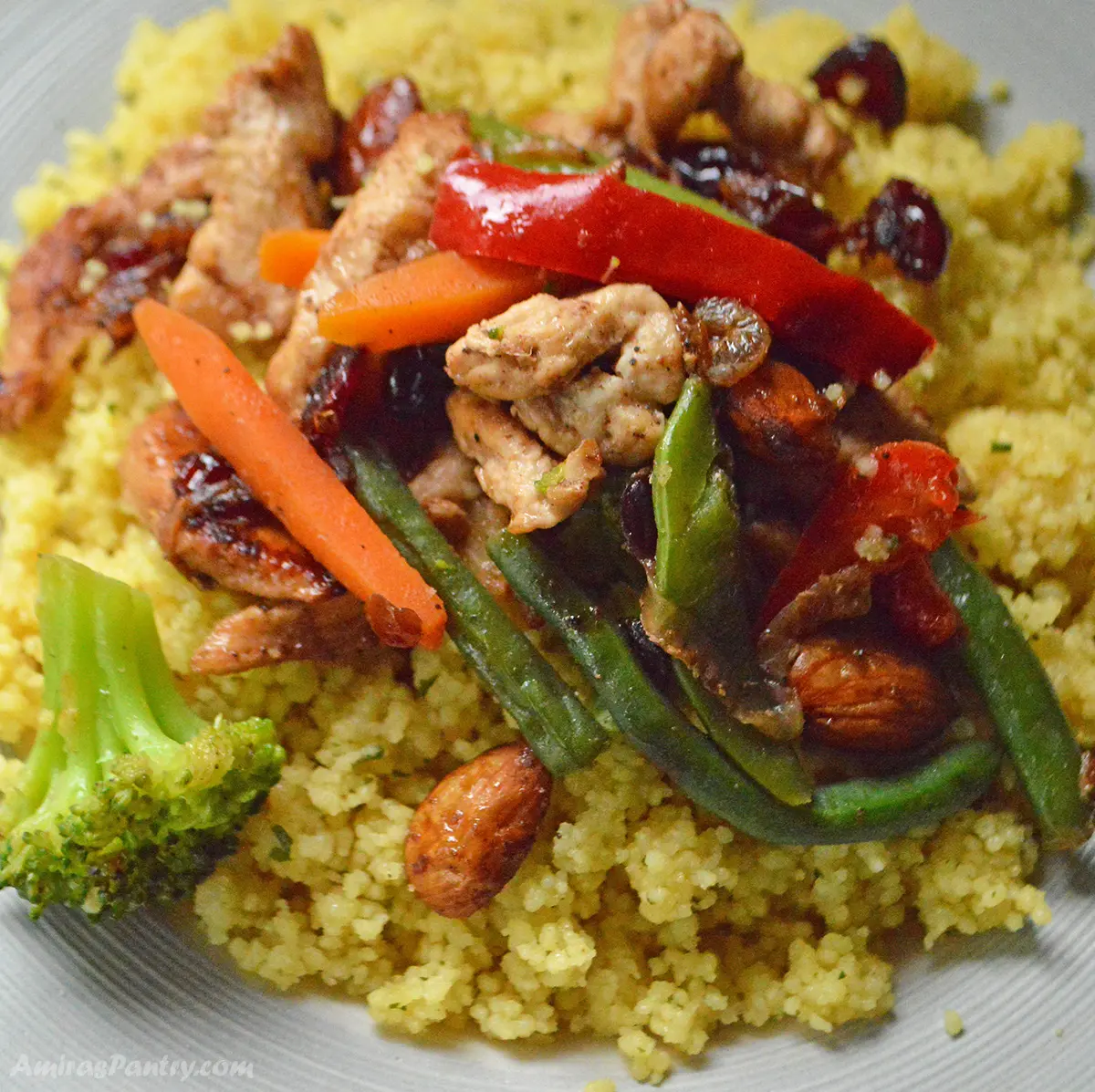 A close up look at a dish with yellow couscous, chicken and vegetables.