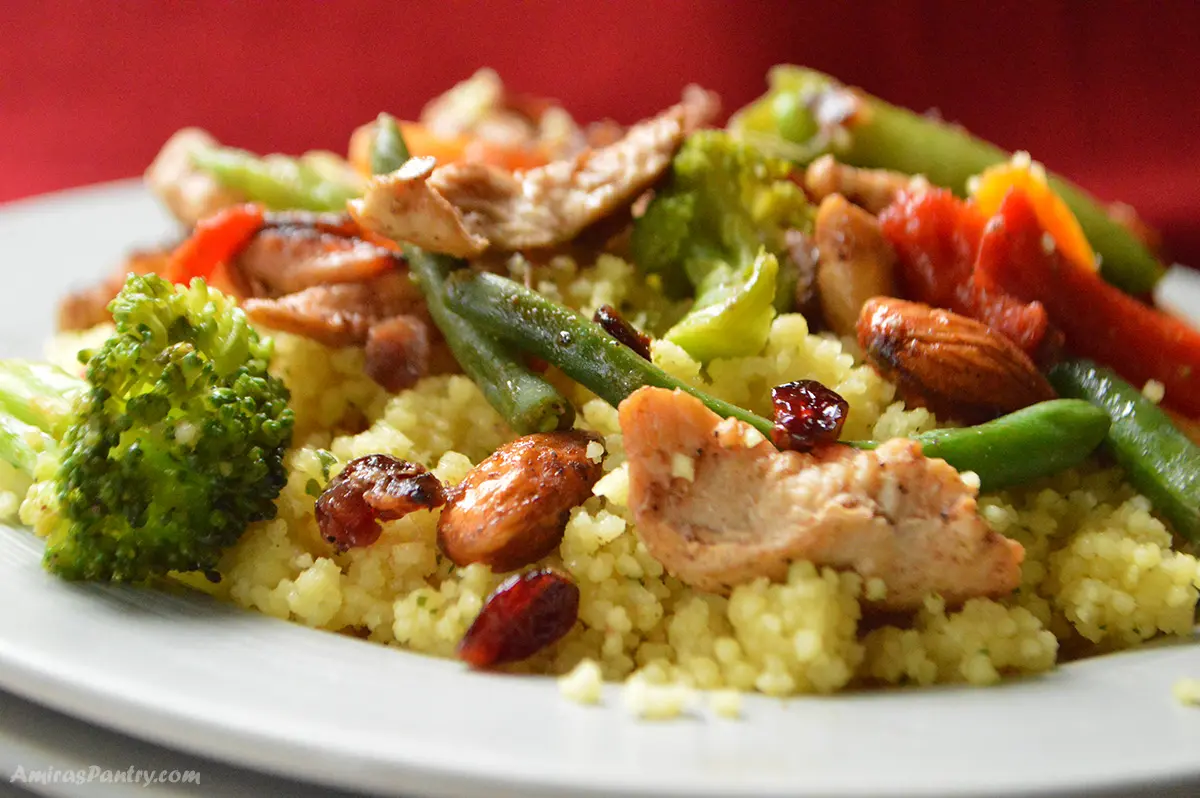 A close up look at a dish with yellow couscous, chicken and vegetables on a white plate.