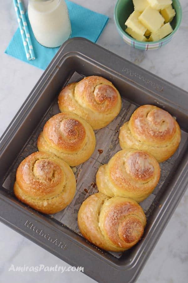 A baking tray with 6 sweet buns with a small plate of butter and a milk bottle on the back.