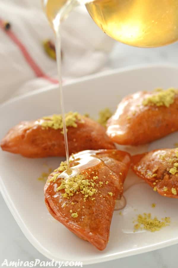 Syrup is poured over qatayef in a white platter.