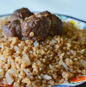 Cooked maftoul on a plate topped with meat.