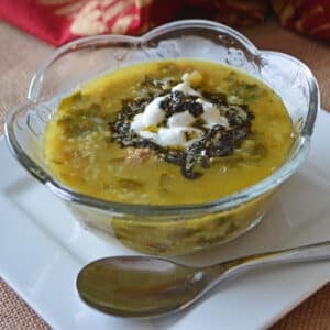 A glass bowl with persian soup and a spoon on the side.