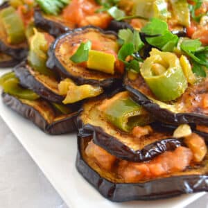 A white plate with eggplant slices with garlic.