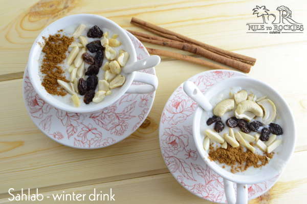 Two cups of Sahlab drink with raisins and nuts, sitting on a wooden table