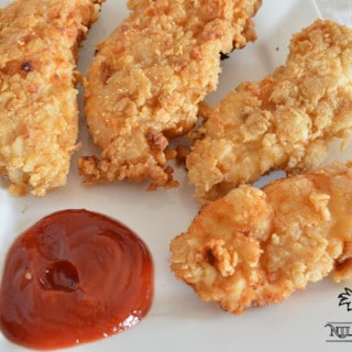 A close up of a plate with chicken strips and ketchup
