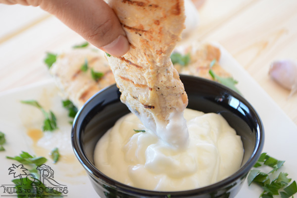 A bowl of garlic dip with hand holding chicken strip