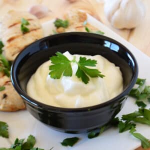 A black bowl with toum garnished with parsley.