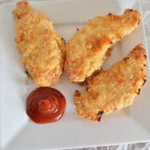 Oved fried chicken tenders on a white plate with ketchup.