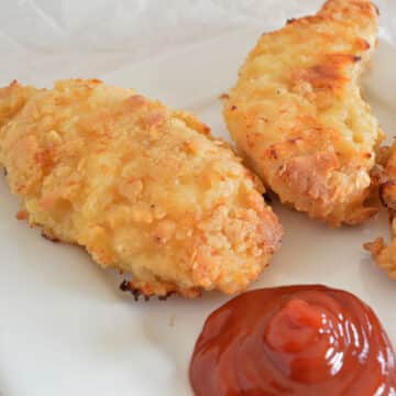Oved fried chicken tenders on a white plate with ketchup.
