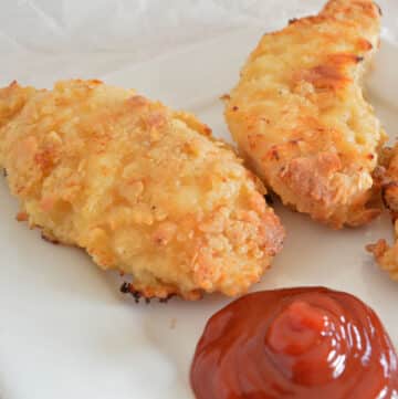 Oved fried chicken tenders on a white plate with ketchup.