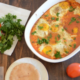 A bowl of food on a table, with Shakshouka and bread