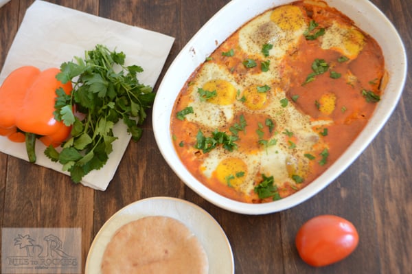 A bowl of food on a plate, with Shakshouka showing beans, bread and eggs