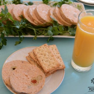 A plate with a cut chicken roll slices and olives, a cup of orange juice
