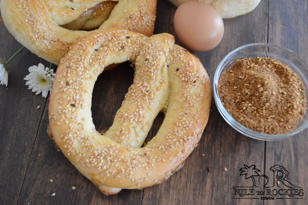 A Simit bread sitting on top of a wooden table with spiced and egg