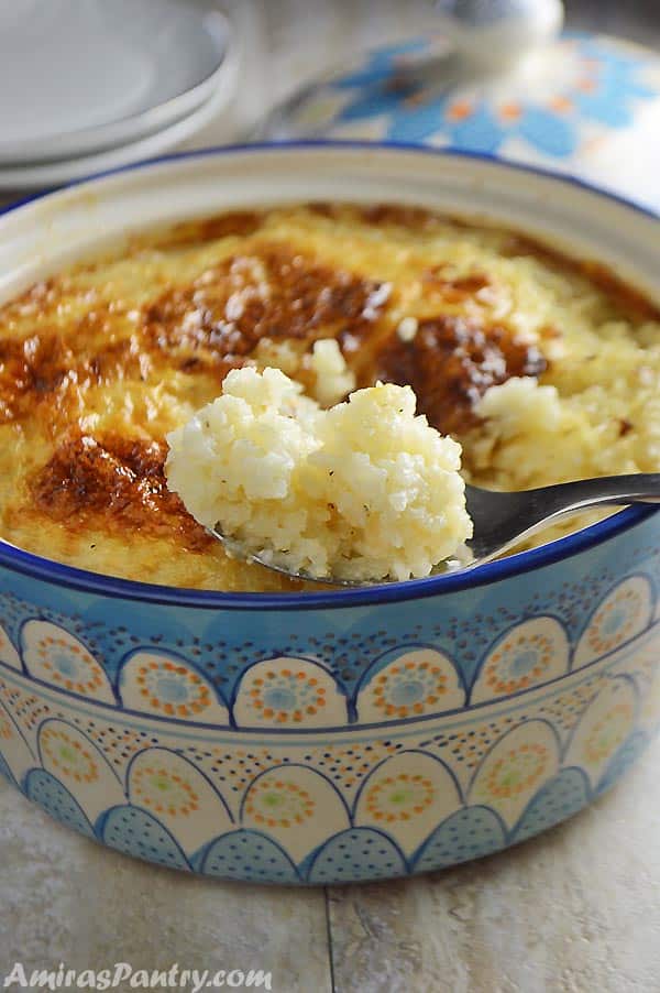 A close up of a bowl of food, with Rice pudding and spoon