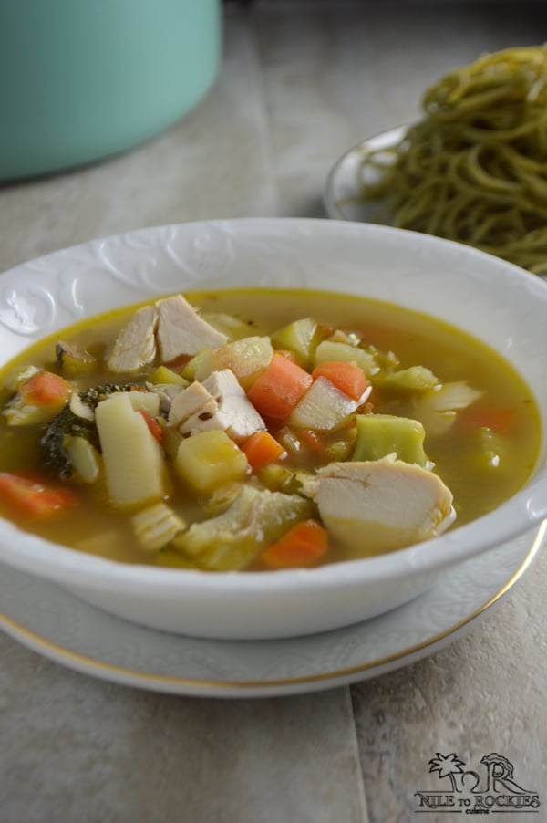 A bowl of soup on a plate, with chicken and vegetables