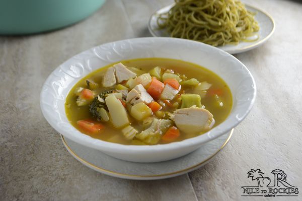 A bowl of soup on a plate, with chicken and vegetables