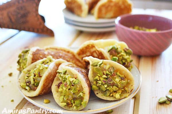 a white plate with qatayef stuffed with cream with other plates of qatayef in the back