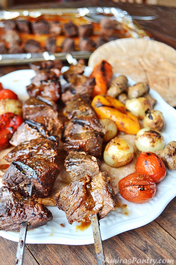 A white plate with shish kabob skewers along with some grilled veggies.