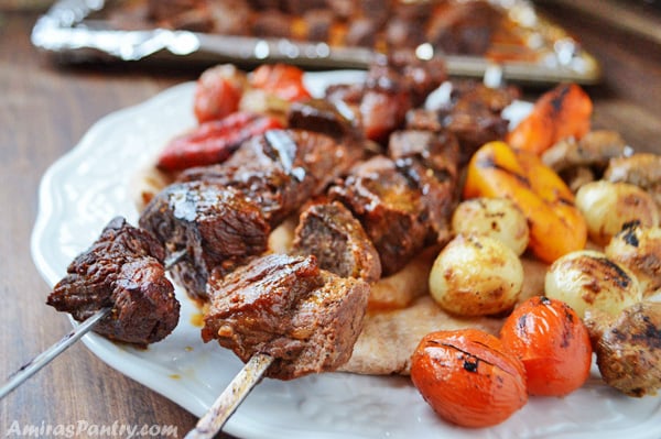 A white plate with middle east shish kabob along with some grilled veggies
