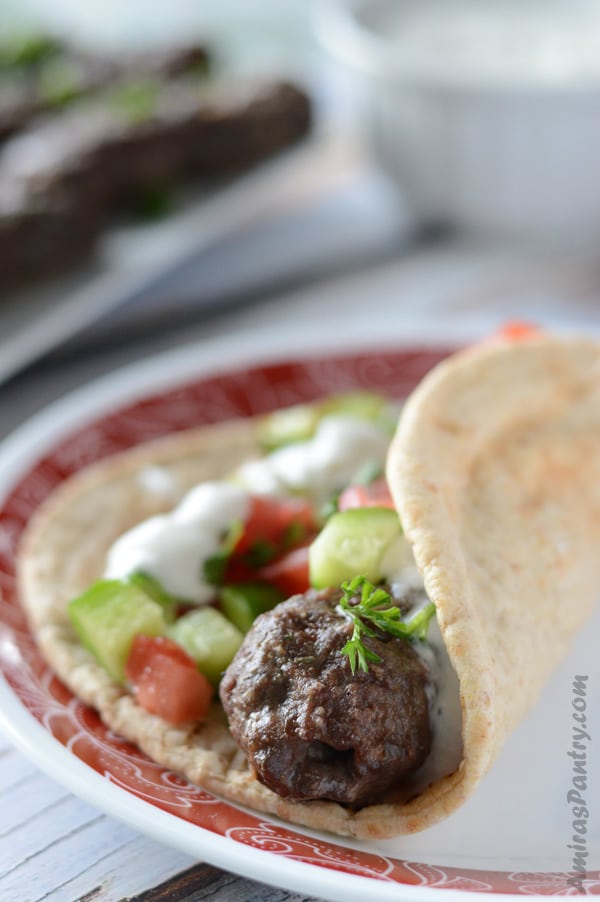 A kofta finger wrapped in pita bread and topped with salad and tzatziki sauce