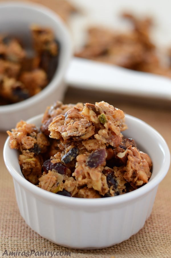 A ramekin in focus heaped with baklava granola chunks with another ramekin at the background.