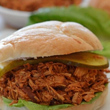 pulled chicken sandwich on a white plate with lettuce leaves in the back