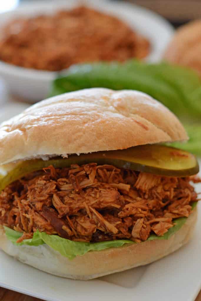 pulled chicken sandwich on a white plate with lettuce leaves in the back
