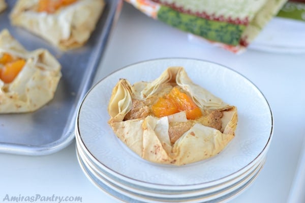 A pumpkin egg-less frangipane tart on a stack of white plates with a sheet pan on the back