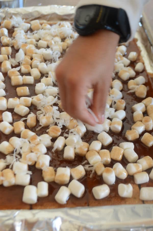 A photo showing a pan with biscuits, Marshmallow and a hand