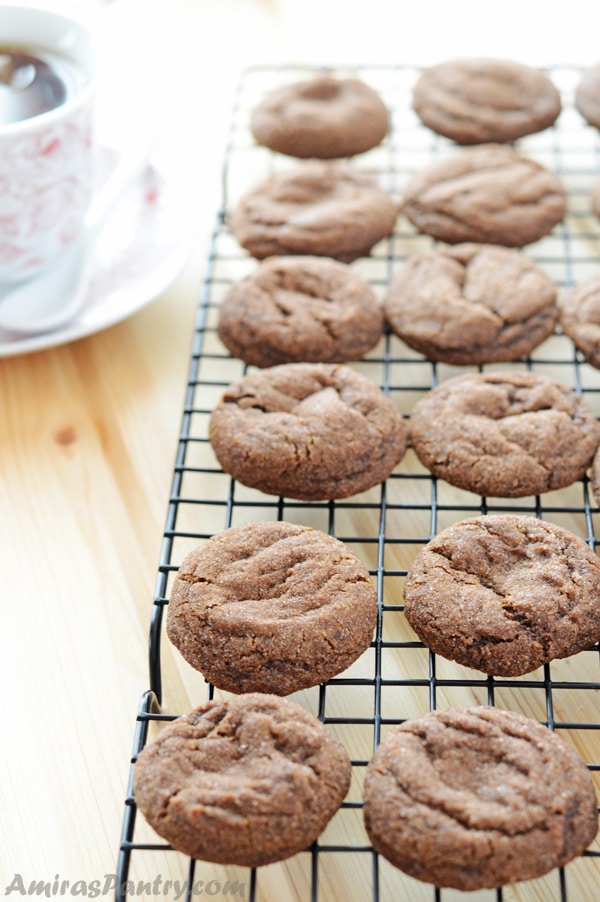 Soft and chewy ginger flavored molasses cookies spread on a cooling rack with a sup of coffee next to it.