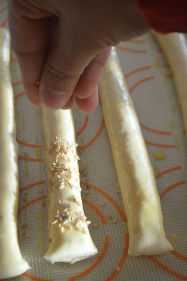 A hand sprinkling sesame over breadsticks
