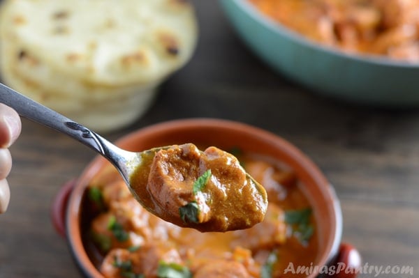 A bowl of food on a table with Chicken tikka and spoon