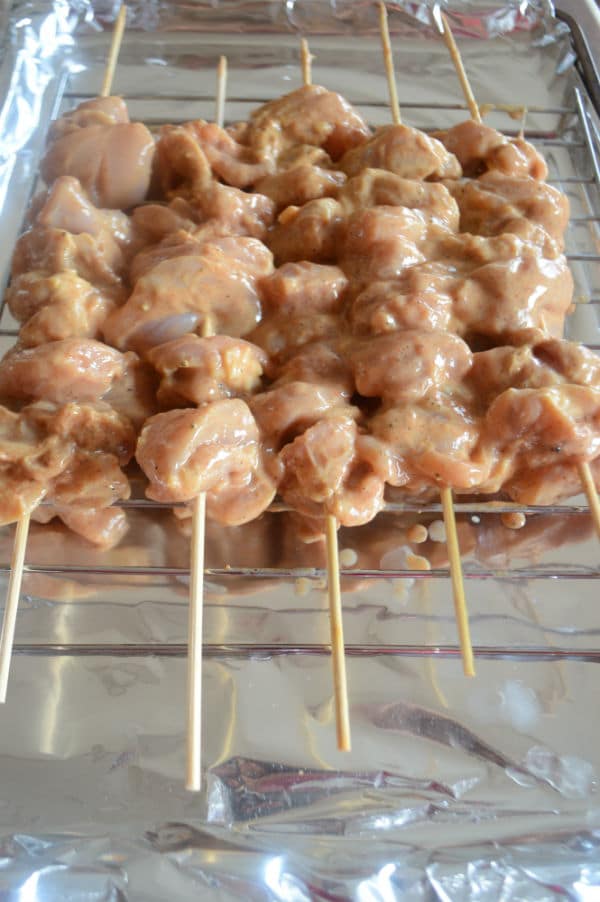 Raw chicken pieces on skewers in a glass pan