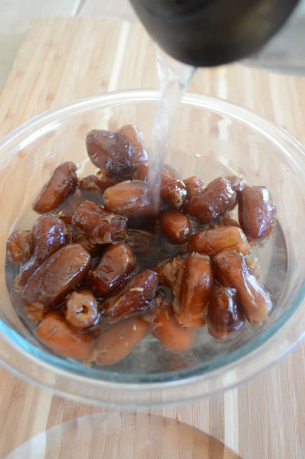 A bowl of food on a board, with dates and water