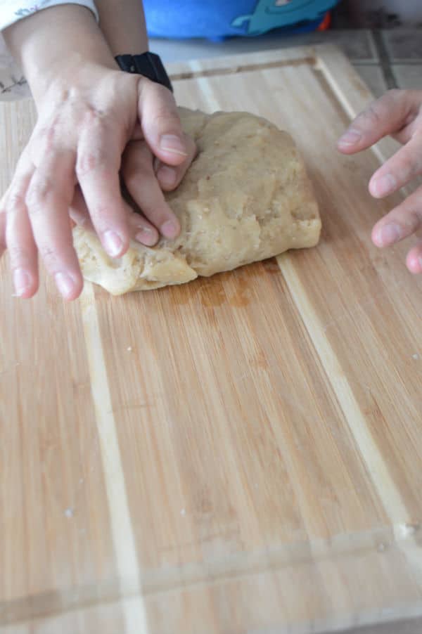 A hand kneading dough on a wooden board