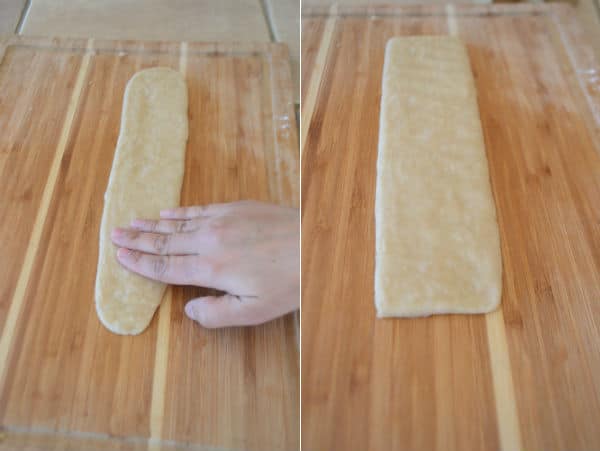 A wooden cutting board, with pieces of dough and hand