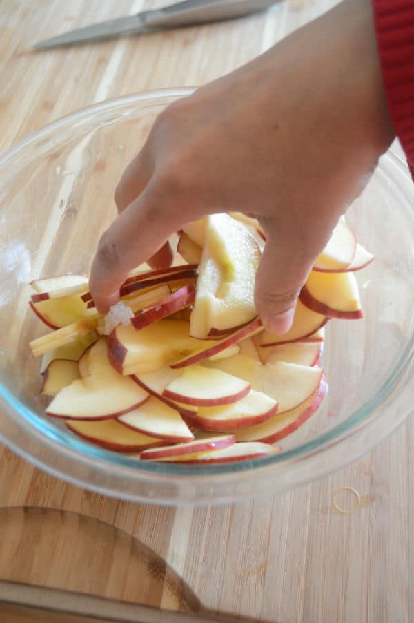 A person holding a plate of food on a table, with Apple cut into slices