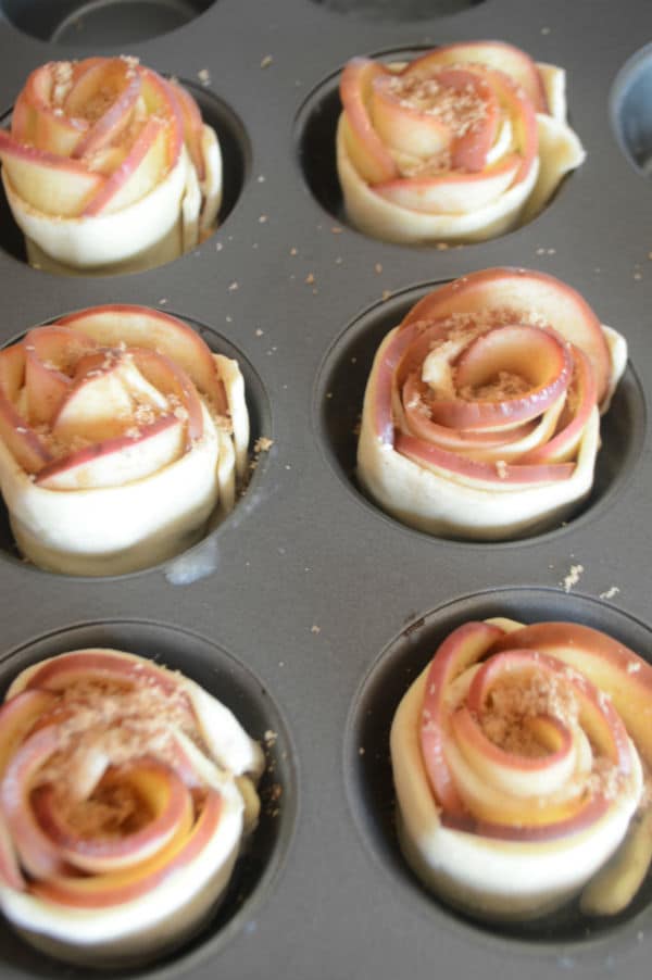 A baking pan with apple slices and dough inside cups
