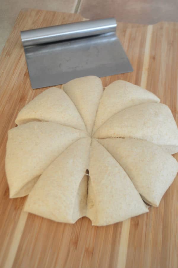 A cut in parts dough sitting on top of a wooden cutting board, with cutting tool