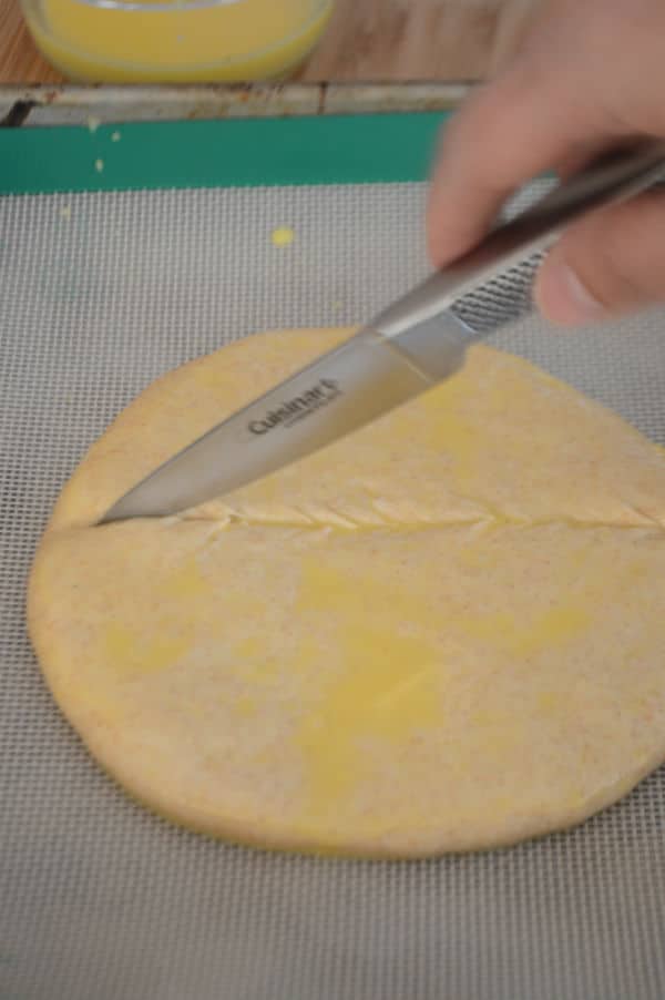 A close up of a round dough on a paper sheet and hand holding knife