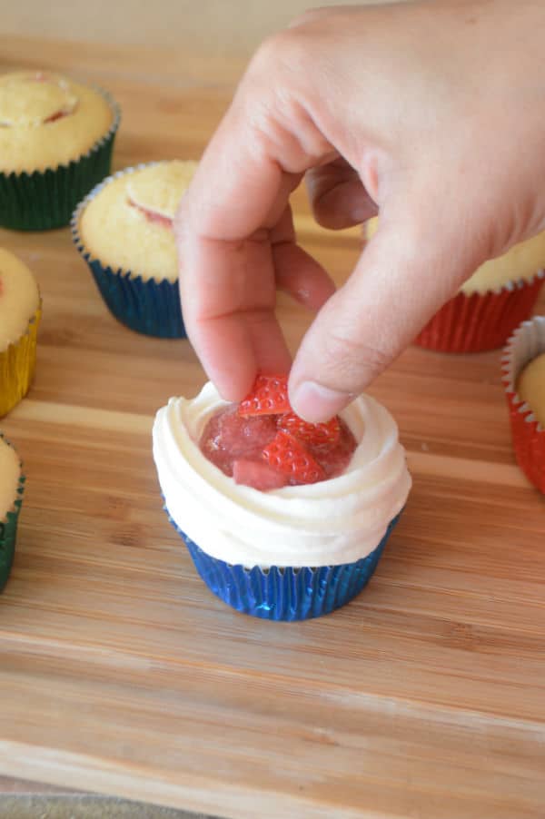 A wooden board with a Cupcake and Strawberry filling with hand