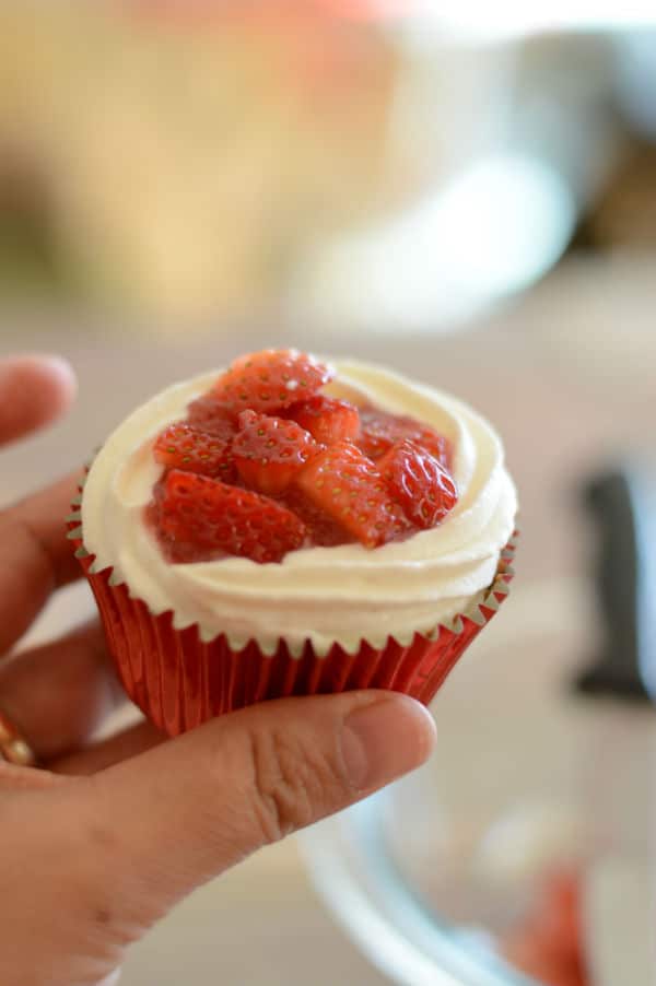 A hand holding cupcake with strawberry and frosting