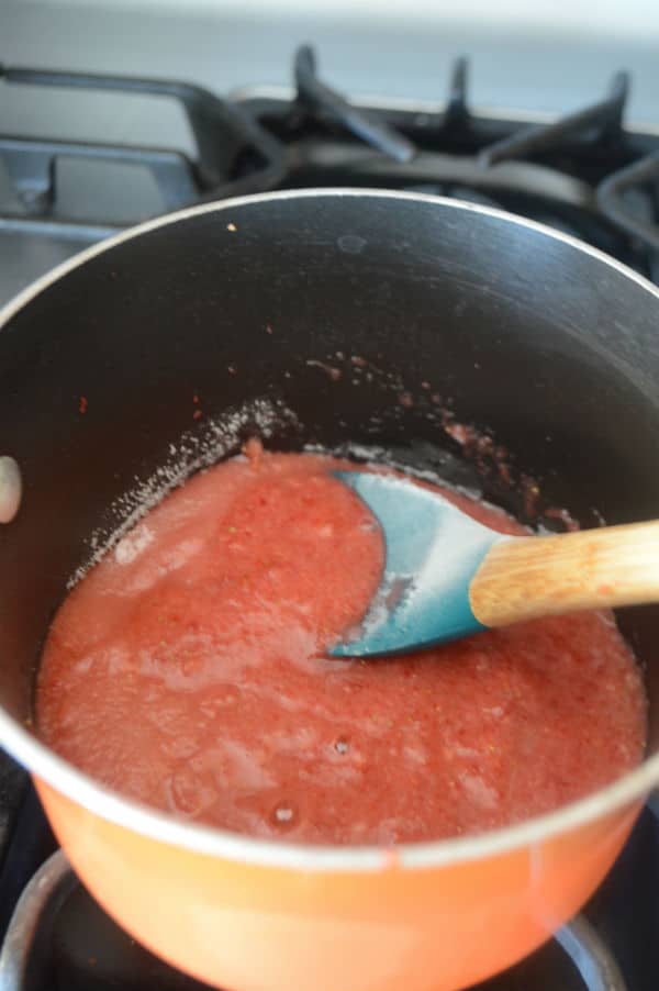 A metal pan on a stove, with Strawberry juice and spoon