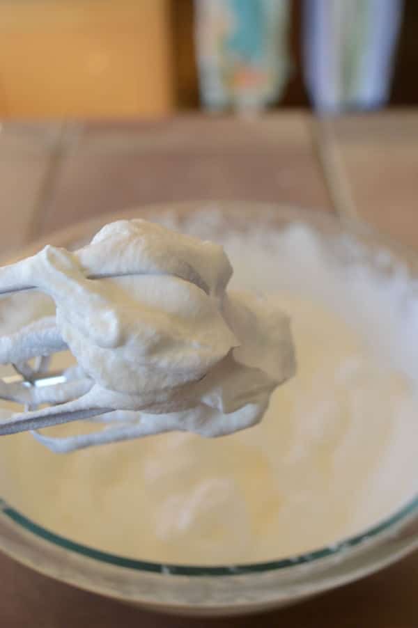 A bowl of dough on a plate on a table and spoon showing dough